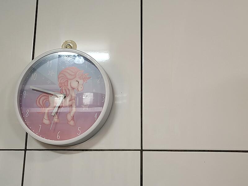 Die pinke Einhorn-Uhr hängt an der Wand über dem Herd und hebt sich von der weißen Fliesenwand ab.