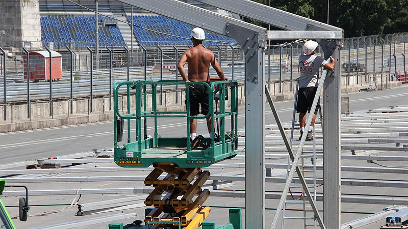 Zwei Bauarbeiter werkeln am Ger&uuml;st f&uuml;r das Boxengeb&auml;ude des Norisrings.