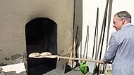 Landrat Alexander Tritthart schiebt beim M&uuml;hlentag in Lonnerstadt ein Brot in den Backofen.