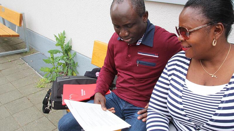 Martins und Bolanle Lawani blicken in ihren Arbeitsvertrag. Sie sitzen vor dem Altenheim in Herzogenaurach, in dem sie tätig waren.