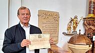 Kirchenf&uuml;hrer Oswald Purucker zeigt ein Echtheitszertifikat aus dem Jahre 1791, dessen Geheimnis er nach vielen Jahren mit Hilfe von k&uuml;nstlicher Intelligenz auf seinem Handy aufkl&auml;rte. Dahinter ist die Grabsteininschrift (Epitaph) der Bayreuther H...