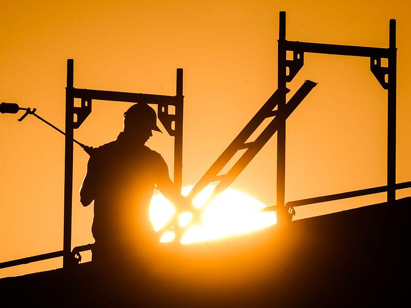Ein Bauarbeiter im Gegenlicht der Sonne auf einem Gerüst Ein Bauarbeiter im Gegenlicht der Sonne auf einem Gerüst
