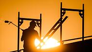 Ein Bauarbeiter im Gegenlicht der Sonne auf einem Ger&uuml;st