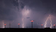 Blitze erleuchten den Himmel zwischen Windrädern