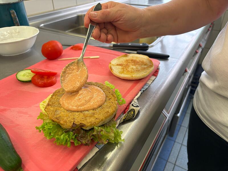 Auf die richtige Reihenfolge kommt es an: Untere Br&ouml;tchenh&auml;lfte, Burgersauce, Salat, Patty, Burgersauce, Gurken- und Tomatenscheiben, obere Br&ouml;tchenh&auml;lfte