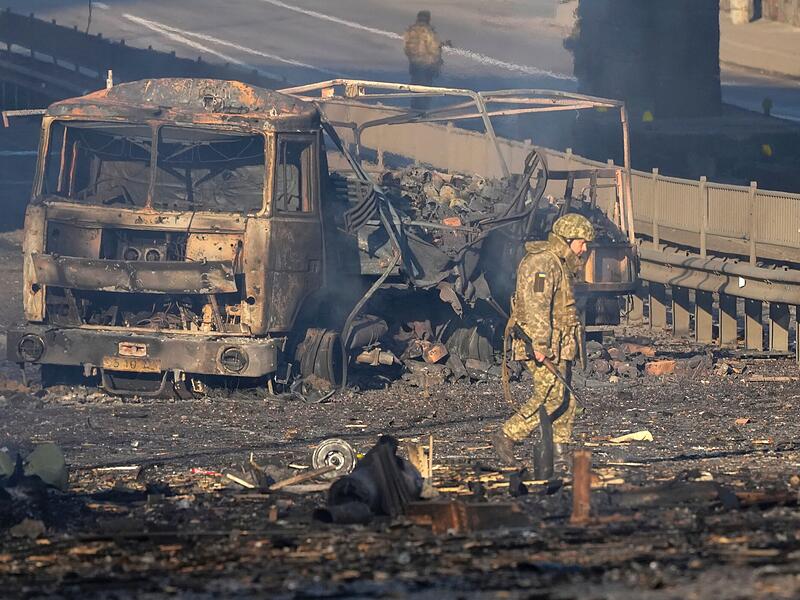Ein ukrainischer Soldat geht an den Trümmern eines ausgebrannten Militärlastwagens vorbei. Russische Truppen haben den erwarteten Angriff auf die Ukraine gestartet und drangen in die Hauptstadt Kiew vor.