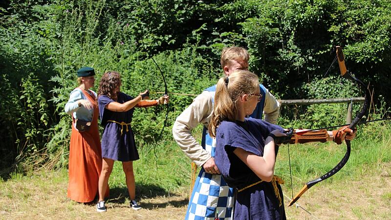 Lady Doria von Sievershof (hinten l.) und Sir Jonas von Wolfenstein (2. von r.) üben mit ihren jungen Besuchern das Bogenschießen im Burggraben, das feindlich Gesinnte auf Distanz halten soll.