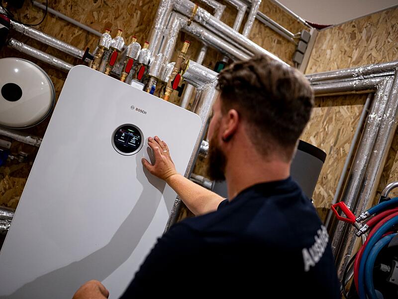 Handwerker zeigt an einer W&auml;rmepumpe auf die Anzeige