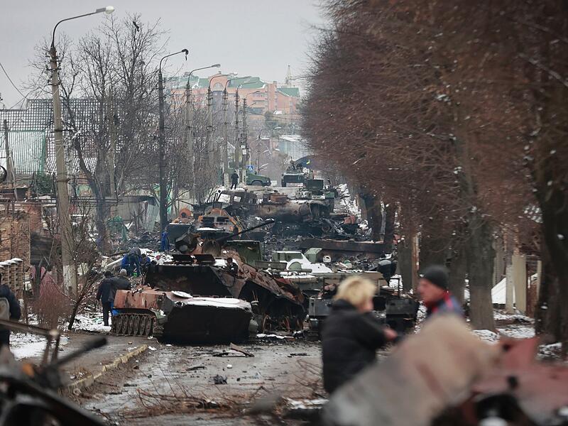 Menschen betrachten die ausgebrannten Überreste russischer Militärfahrzeuge auf einer Straße in der Stadt Bucha in der Nähe der ukrainischen Hauptstadt Kiew.