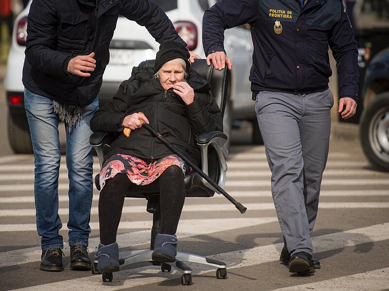 Grenzpolizisten schieben eine ältere Dame in einem Bürostuhl an der ukrainischen-moldauischen Grenze. Wegen des russischen Angriffs auf die Ukraine sind nach Angaben des UN-Flüchtlingshilfswerks (UNHCR) etwa 368 000 Menschen auf der Flucht.