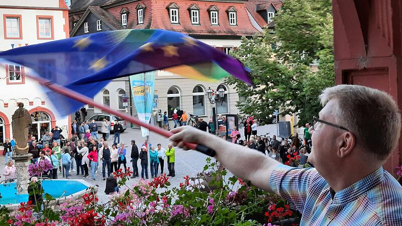 Der Volkacher Sebastian Kleinau schwenkte kurz vor Beginn der Stadtratssitzung die Europaflagge mit Regenbogen vom Rathausbalkon, um seine Solidarit&auml;t mit Gefl&uuml;chteten zu zeigen. Unten auf dem Marktplatz hatten sich Gegner des geplanten Fl&uuml;chtlingsheims versammelt.