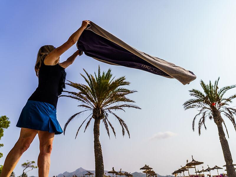 Eine Frau breitet am Strand ihr Handtuch aus Eine Frau breitet am Strand ihr Handtuch aus
