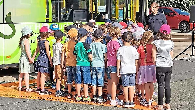 Polizeibeamter i.&nbsp;R. Helmut F&ouml;rtsch (rechts) verdeutlicht die Gefahr des toten Winkels am Schulbus. Alle Kinder, die auf der rot markierten Fl&auml;che stehen, sind nicht vom Omnibusfahrer zu sehen.