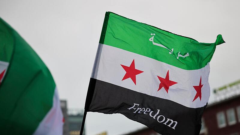 Feiernde schwenken die Flagge der syrischen Revolution vor dem Hauptbahnhof in Duisburg.