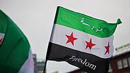 Feiernde schwenken die Flagge der syrischen Revolution vor dem Hauptbahnhof in Duisburg.