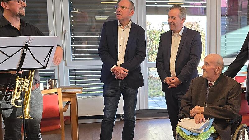 Peter Wei&szlig;, Leiter des Bl&auml;serensembles der Musikschule Hemhofen (l.), gratuliert Georg Huber (im Rollstuhl). Dahinter stehen Gerhard Wagner, 2. B&uuml;rgermeister von Hemhofen (l.), und Landrat Alexander Tritthart.