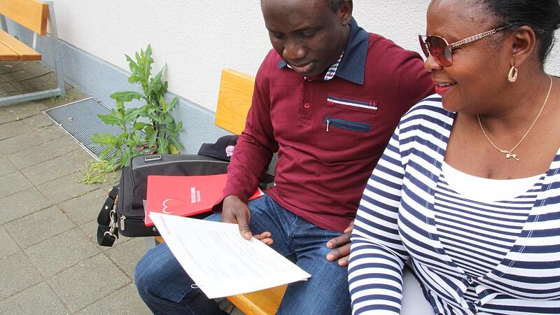 Martins und Bolanle Lawani blicken in ihren Arbeitsvertrag. Sie sitzen vor dem Altenheim in Herzogenaurach, in dem sie t&auml;tig sind.