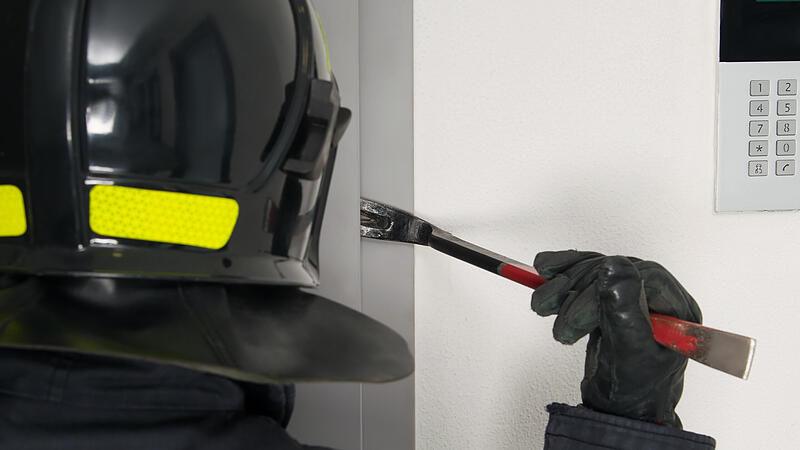 Ein Feuerwehrmann &ouml;ffnet eine verschlossene T&uuml;r (Symbolfoto).