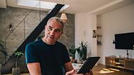 Ein Mann sitzt mit einem Tablet am Tisch