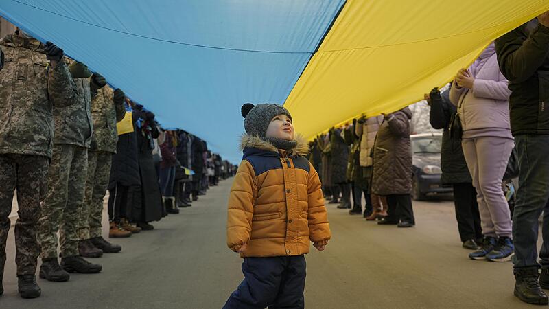 Ein Kind geht unter einer langen ukrainische Fahne, die durch das Olympiastadion in Kiew getragen wird. Nach Warnungen vor einem  bevorstehenden russischen Einmarsch in die Ukraine, rief der ukrainische Pr&auml;sident Zelenskyy zu einem Tag der Einheit auf.