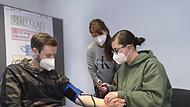 Anna Maria Trager (rechts) übt das Blutdruckmessen an Valentin Rau, Auszubildender im Diakonie-Seniorenzentrum Hephata, im Skills Lab der Diakoniestation Drei-Franken-Eck unter den wachsamen Augen von Praxisanleiterin Michaela Wagner.