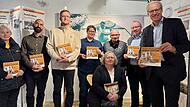 Bei der &Uuml;bergabe der Begleitbrosch&uuml;re in Herzogenaurach (von links, stehend): Julie K&auml;hler (Herzo-&Uuml;bersetzerin), Mischa Szeker (Adidas Schweiz), Ulrich Planer (Puma), Susen Friedrich (Adidas), Helmut Fischer (Puma), Christian Hoyer und German Hacker, vorne sitzend: Sigrid Dassler