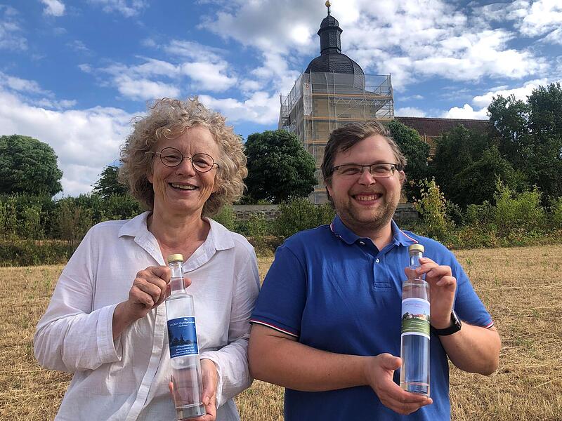 Pfarrerin Doris Otminghaus und Vertrauensmann Daniel Herterich stellen den „Jubiläumsbrand Pastorenbirne“ vor. Im Hintergrund ist die eingerüstete Bergkirche zur Heiligen Dreifaltigkeit zu sehen.