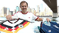 Adidas-CEO Bj&oslash;rn Gulden h&auml;lt bei einer Presseveranstaltung im Juni 2026 zur WM in New York die Trikots der deutschen Nationalmannschaft in die Kamera. F&uuml;r den Sportartikelhersteller ist das Mega-Event ein Milliardengesch&auml;ft.