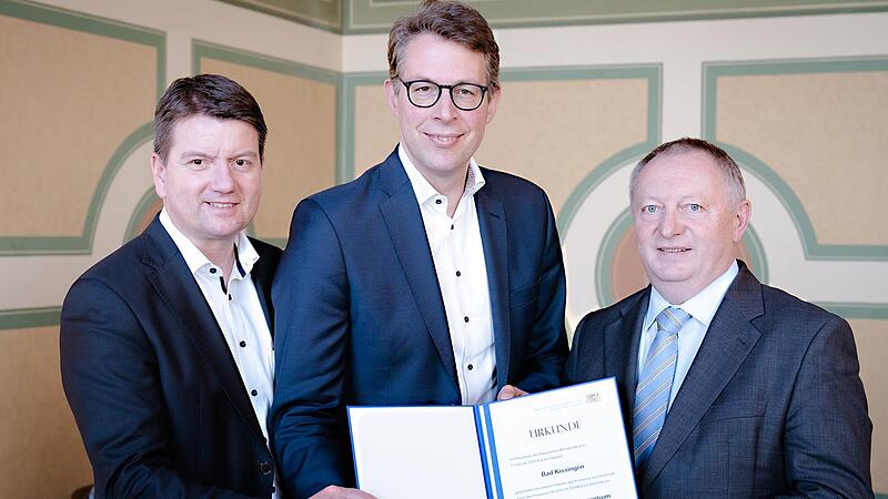 Unser Bild zeigt Staatssekret&auml;r Sandro Kirchner (links) und Landrat Thomas Bold (rechts), die von Wissenschaftsminister Markus Blume die entsprechende Urkunde &uuml;berreicht bekommen.