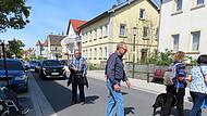 Die dunkelgrauen Längsrillen auf der linken Seite am Gehsteig zeigen eine Querungsmöglichkeit an - Die Gruppe überquert die Bahnhofstraße in Höhe des Optikers.