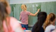 Eine junge Lehrerin schreibt an eine Schultafel im Mathematikunterricht an einer Gesamtschule.