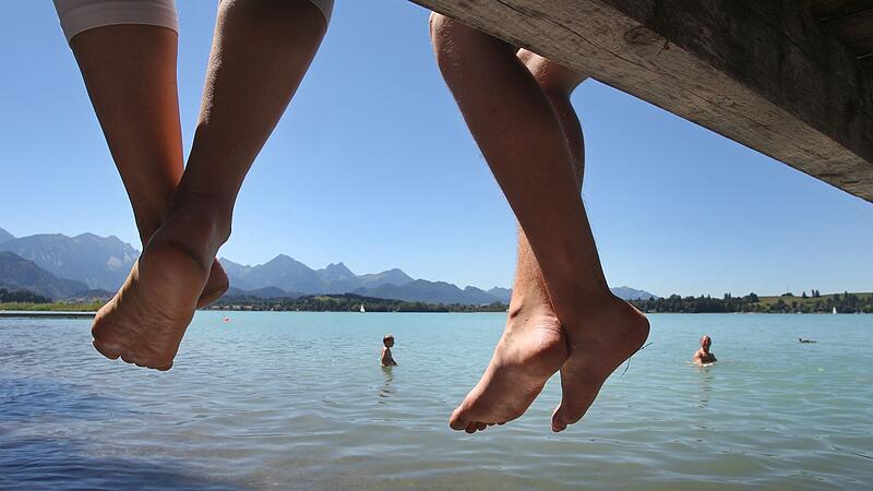 Badegäste lassen auf einem Steg am Forggensee Ihre Beine baumeln Badegäste lassen auf einem Steg am Forggensee Ihre Beine baumeln