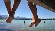 Badegäste lassen auf einem Steg am Forggensee Ihre Beine baumeln Badegäste lassen auf einem Steg am Forggensee Ihre Beine baumeln