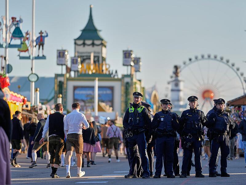 Besucher gehen, beobachtet von Polizeibeamten, nach dem Einlass wieder auf das Gelände des Oktoberfests. Nach der Schließung wegen einer Bombendrohung ist das Münchner Oktoberfest am Mittwochabend wieder geöffnet worden.