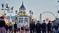 Besucher gehen, beobachtet von Polizeibeamten, nach dem Einlass wieder auf das Gelände des Oktoberfests. Nach der Schließung wegen einer Bombendrohung ist das Münchner Oktoberfest am Mittwochabend wieder geöffnet worden.