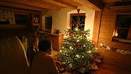 Familie sitzt vor einem beleuchteten Weihnachtsbaum