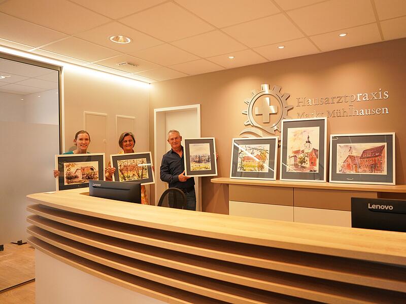 Frauke Kosteletzky, K&uuml;nstlerin Ulrike Polifke und Gr&uuml;ndungsmitglied der B&uuml;rgergenossenschaft Markt M&uuml;hlhausen Reinhard Klaus (von links) mit den Kunstwerken  in der Praxis. in M&uuml;hlhausen.