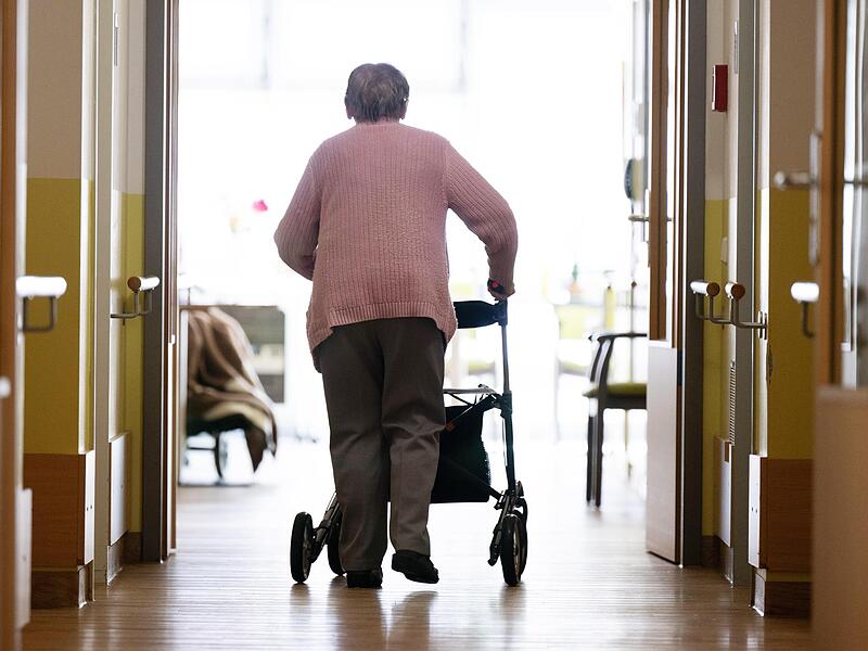 Eine Frau geht mit einem Rollator in einem Pflegeheim den Gang entlang. Eine Frau geht mit einem Rollator in einem Pflegeheim den Gang entlang.
