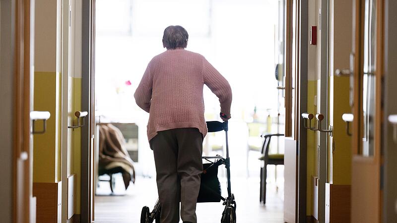 Eine Frau geht mit einem Rollator in einem Pflegeheim den Gang entlang.