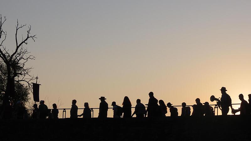 Im Gegenlicht der aufgehenden Sonne geht der Pilgerzug über die Alte Saalebrücke in Euerdorf.