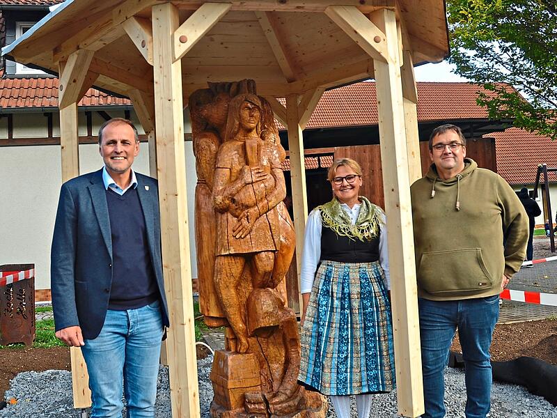Die Holzskulptur der sagenumwobenen &bdquo;Knellesjungfern&ldquo; von Erwin Fehn hat in einem Pavillon vor der Zecher-Halle ein neues Zuhause gefunden. Dar&uuml;ber freuen sich, von links, B&uuml;rgermeister Daniel Wei&szlig;erth, die Vorsitzende des Volkstrachtenvereins &bdquo;Ze...