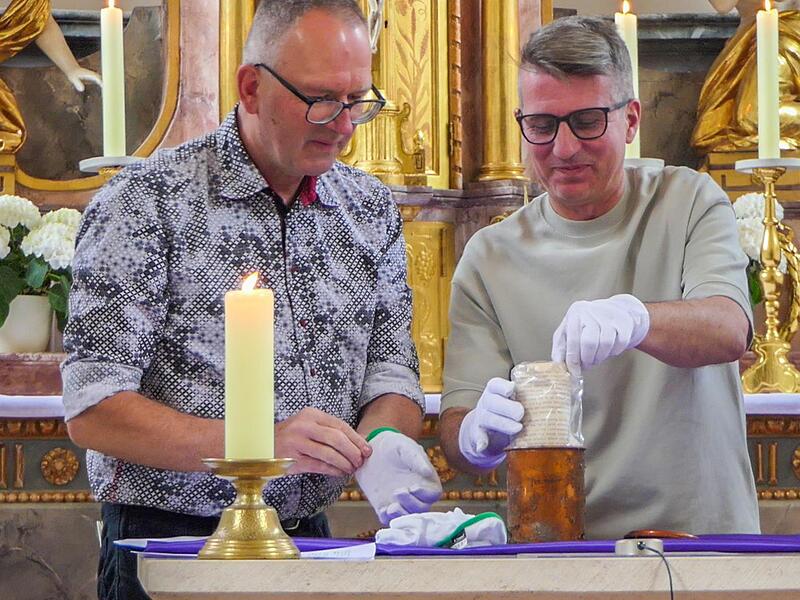 K&uuml;ster Manfred Vogt und Pfarrgemeinderat Stefan Kamm (rechts) &ouml;ffneten die Zeitkapsel, in der ein altes Dokument steckte.