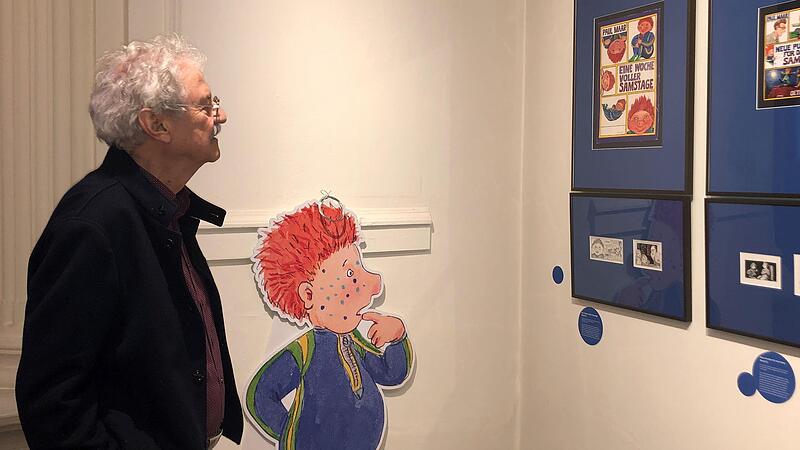 Paul Maar betrachtet mit seiner bekanntesten Figur, dem Sams, Werke in seiner Ausstellung.