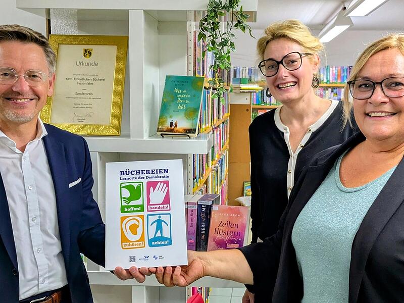 Tobias Reiß, Vizepräsident des Bayerischen Landtags, überreicht die Aktionsplakette „Büchereien: Lernorte der Demokratie“ an Sabine Jentsch (rechts), Leiterin der Bücherei Sassanfahrt. Mit dabei: Dr. Claudia Maria Pecher (Mitte), Leiterin der Landesfachstelle für Büchereien und Bildung.